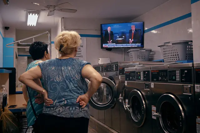Women stand inside a Brooklyn laundromat as they watch the broadcast of the meeting between Russian President Vladimir Putin and US President Donald Trump (who are seated) in Alaska.