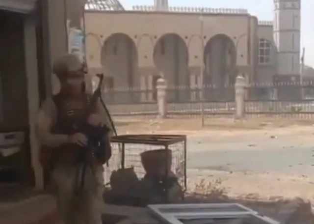 An armed man standing on a road opposite a mosque