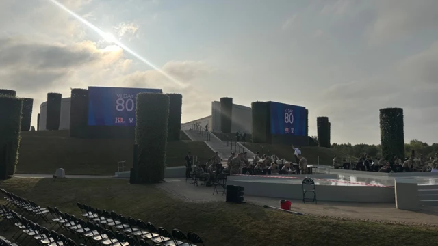 Part of the ceremony viewing area, you can see big screens which say VJ Day 80 at the back and military personnel in uniform in the foreground
