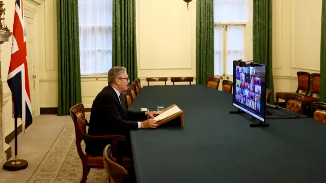 Stramer sits in front of a TV screen filled with members of the coalition of the willing