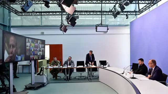 Volodymyr Zelensky sits at desk next to the German chancellor with a group video call on the screen opposite