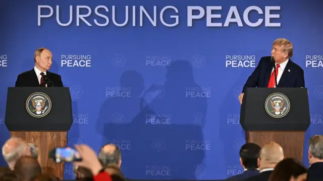 Putin and Trump stood behind podiums a distance apart from each other. Both stood behind microphones. Blue background with text that reads "pursuing peace".