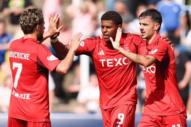 Aberdeen's Kusini Yengi (centre) celebrates with Nicolas Milanovic (R) and Adil Aouchiche after scoring to make it 2-0 during a Premier Sports Cup Second Round match between Greenock Morton and Aberdeen at Cappielow Park