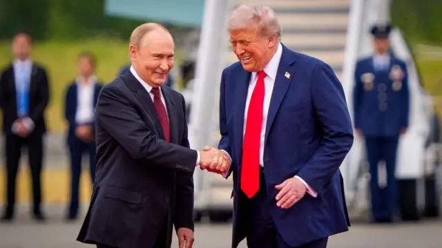 Vladimir Putin shakes Donald Trump's hand. Both are smiling.