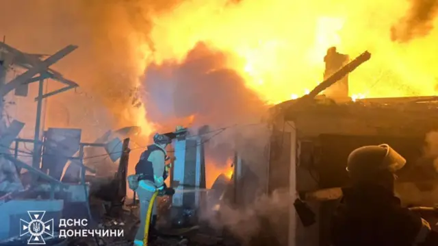 A dark image, taken overnight, which shows emergency services attempting to put out a widespread fire in a building. The flames and smoke reach into the sky