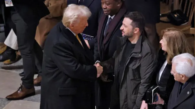 Donald Trump (L) in a black winter coat shakes hands with Volodymyr Zelensky (R) inside Notre Dame de Paris, the daughter of the Italian President of the Republic and the Italian President of the Republic watching the exchange from Zelensky's left