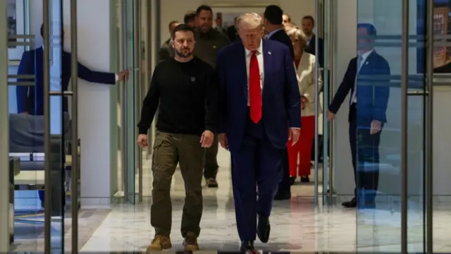 Volodymyr Zelensky stands next to Donald Trump as they walk through glass doors inside Trump Tower