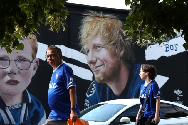 Ipswich Town fans walk past a mural of Ed Sheeran