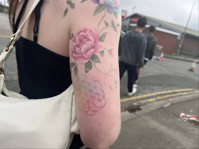 A woman's arm showing colourful floral tattoos and a colourful interlocking circles tattoo.