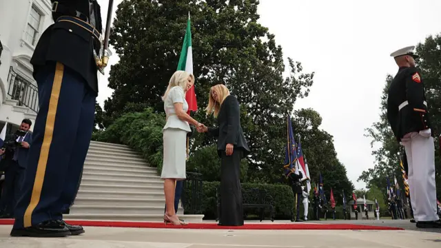 White House head of protocol Monica Crowley (L) in a white cocktail dress shakes hands with Italian Prime Minister Giorgia Meloni, in a black suit, as she arrives to the White House