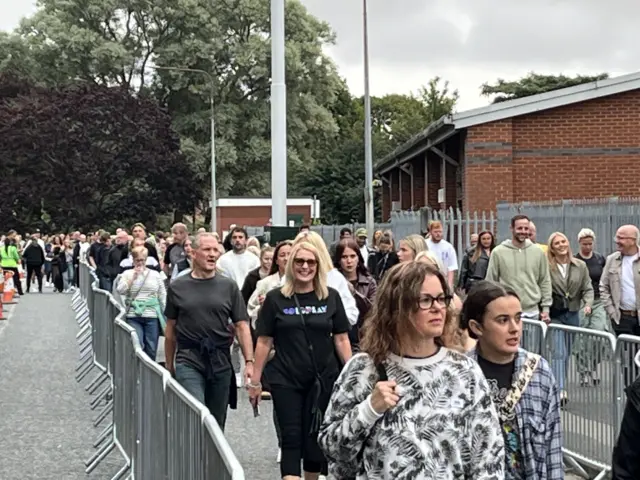 Groups of people walking towards the camera through separated by metal barriers.