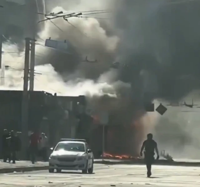 A man and a car on the street in front of a burning building