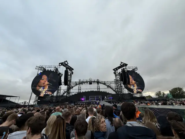 A stage with two circular screens either side showing Ayra Starr performing. Crowds can be seen looking towards the stage.