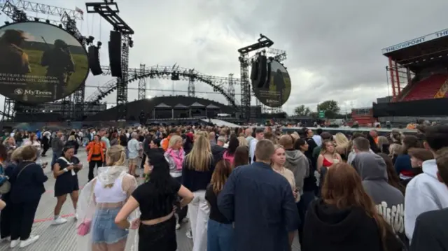 Crowds of people stand in front of a large stage set with two huge circular screens on either side