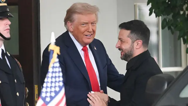 Donald Trump (L) in black suit, white shirt and red tie shakes hands with a smiling Volodymyr Zelensky (R) as he welcomes him on the north portico of the White House