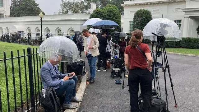 Reporters with umbrellas outside of the White House
