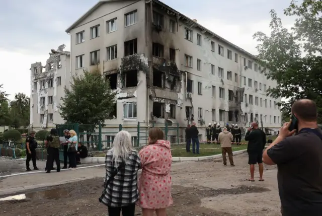 People stand near the site of a drone strike on a residential area in Kharkiv, northeastern Ukraine. Two women are looking at the building which has damaged windows from the strikes