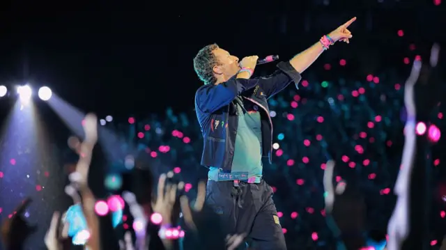 Coldplay lead singer Chris Martin on stage holding microphone and pointing upwards