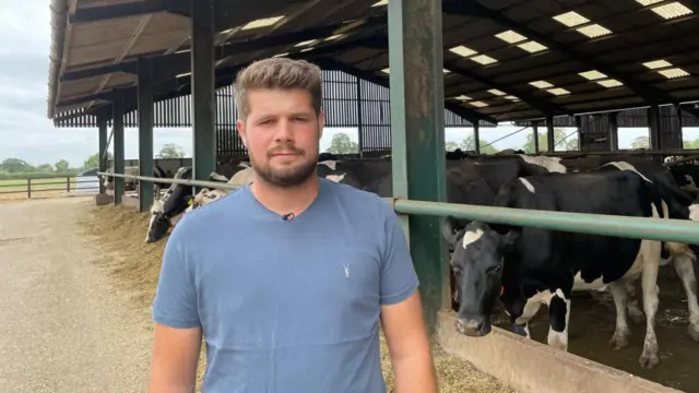 Graham Dutton, a dairy farmer from Marsh House Farm, stands in front of a herd of cows in a barn