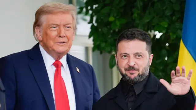 US President Donald Trump is wearing a blue suit and white tie, standing next to Ukrainian leader Volodymyr Zelensky. Zelensky wears a black shirt and black suit jacket, and waves towards the camera.