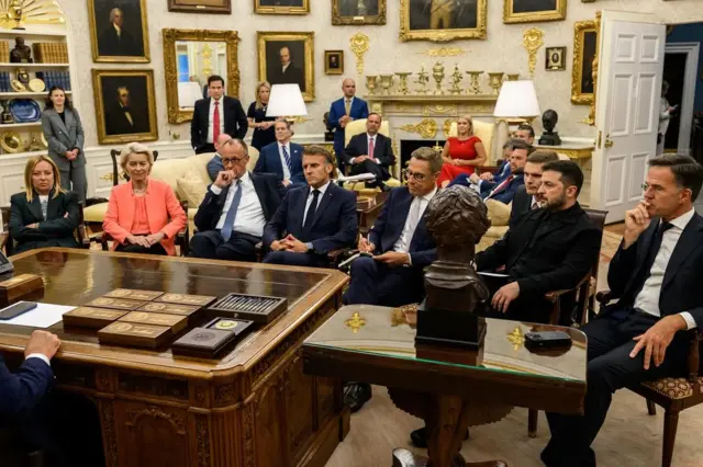 From left to right, we can see Giorgia Meloni, Ursula von der Leyen, Friedrich Merz, Emmanuel Macron, Alexander Stubb, Volodymyr Zelensky and Mark Rutte sat on chairs pulled up around a coffee table in the Oval Office..