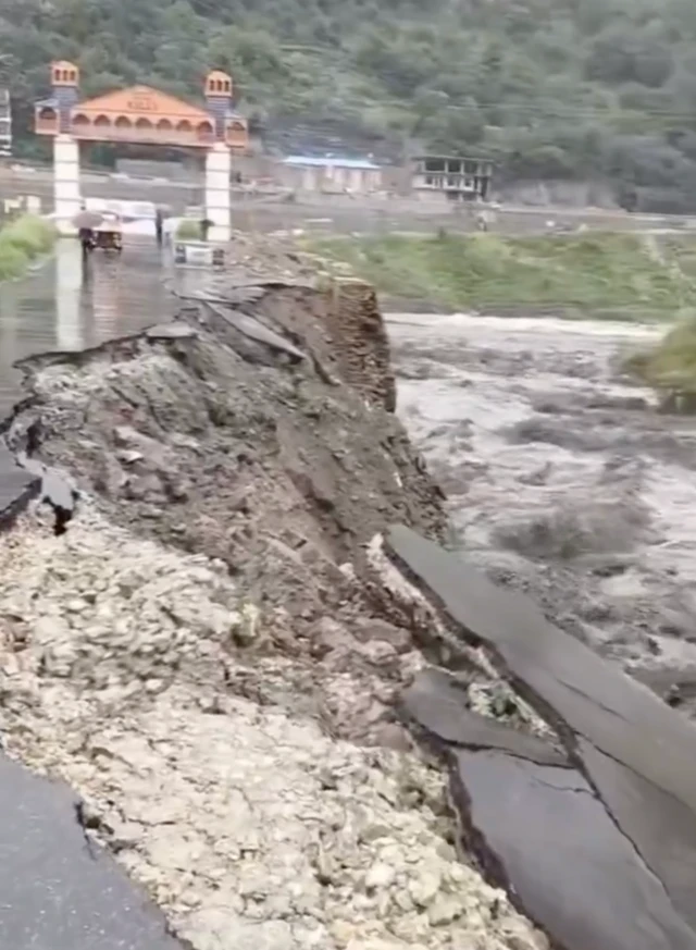 A section of a road that has fallen into a fast-flowing river along a hillsidwe
