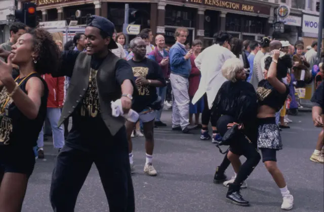 Performers wearing black t-shirts with gold design dancing on Ladbroke Grove during Notting Hill Carnival, London, 1992