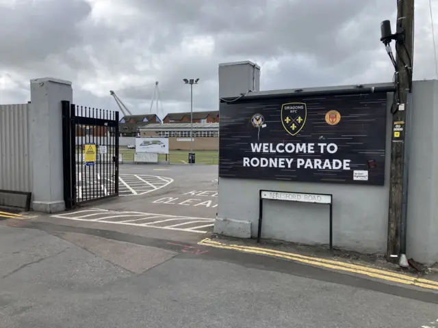 A general view of the entrance of Rodney Park. It shows the gate with a black sign in white writing which says 'Welcome to Rodney Parade'