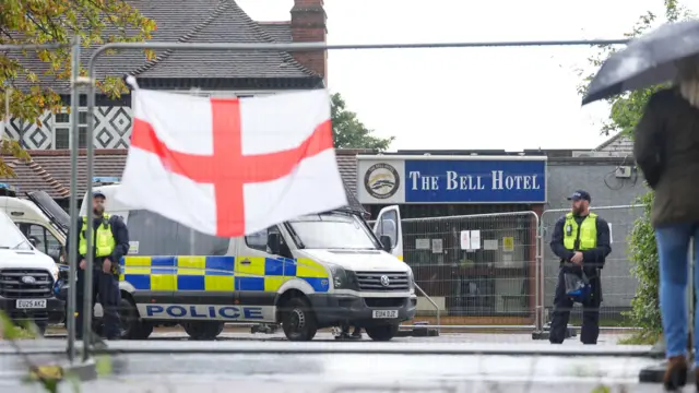 A picture of the bell hotel with police outside and an English flag in the foreground