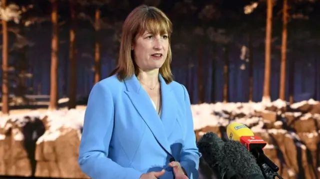 Rachel Reeves in a blue suit, stood behind microphones.