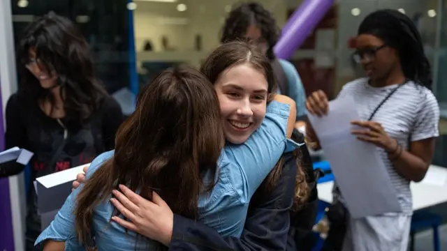 Two female students hug while holding their results envelopes
