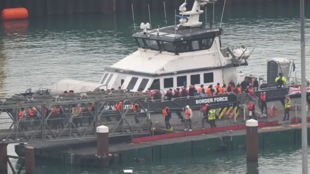 A group of men in orange life jackets walk down a Border Force boat after rescue at sea in the Channel