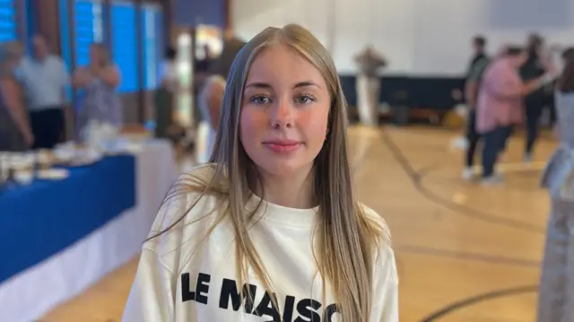Girl standing in gymnasium with people standing, blurry, in the background