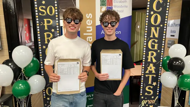 Two boys smile as they look at the camera, holding their results up. They're wearing black sunglasses with 'Class' and '2025' written on them