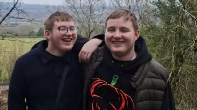 Brothers Jaydan and Jacob are hugging and smiling, whilst standing in the countryside