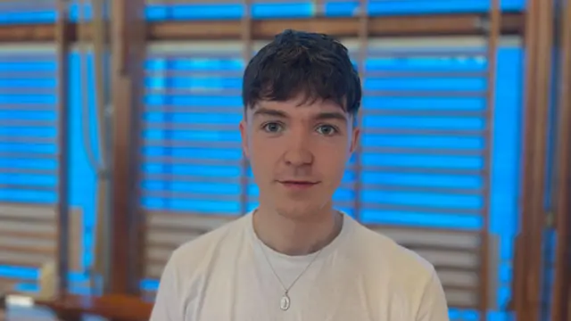 Boy wearing white T-shirt and silver necklace looks into the camers