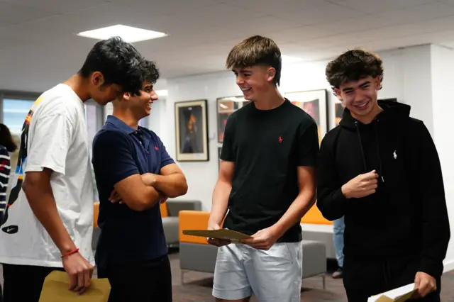 A group of four boys laughing and smiling with their results envelopes in their hands