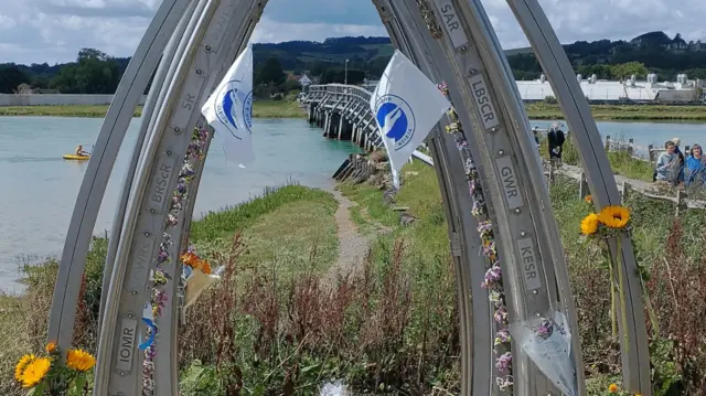 A view of the Old Shoreham Toll Bridge with a memorial covered in flowers