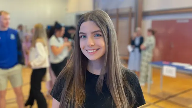 Girl smiles at camera with crowd of people, blurry, standing behind her in the background