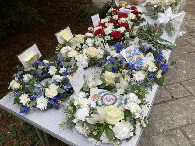 Wreaths with white, red and blue flowers lined up on a table outside a church.
