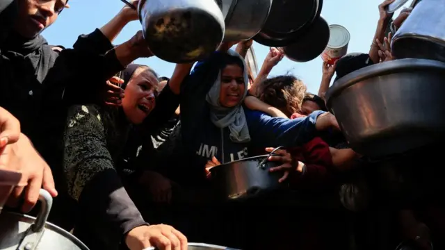 Palestinians hold pots while waiting to receive food from a charity kitchen in Khan Younis, southern Gaza Strip