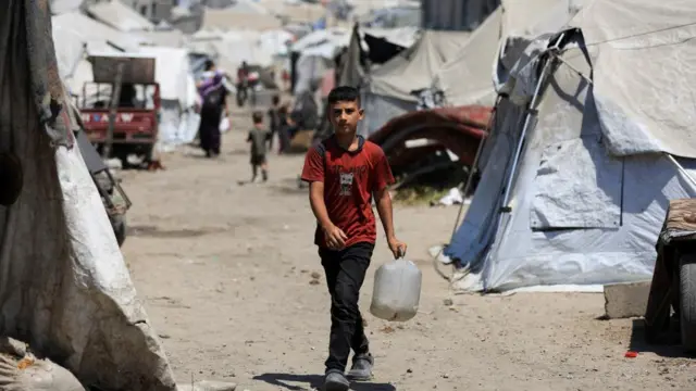 A boy walks with a canister as Palestinians displaced by the Israeli military offensive take shelter in tents
