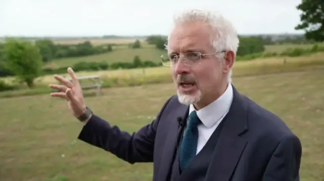 Mid shot of Dominic Oliver, former head teacher of Lancing College standing in a field in a suit