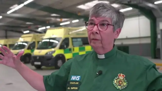 Jill Simpson, a senior chaplain for South East Coast Ambulance Service wearing dog collar over green uniform inside an ambulance station