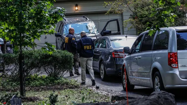FBI officials walk up to Bolton's home next to SUV cars