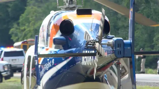 Helicopter landed on grass next to a road in front of vehicles