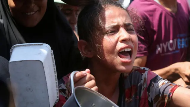 A girl reacts as she and other Palestinians wait to receive food from a charity kitchen in Khan Younis, southern Gaza Strip