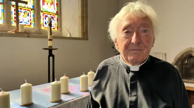 Revd Pat Alden wearing her dog collar inside a church in Shoreham surrounded by candles