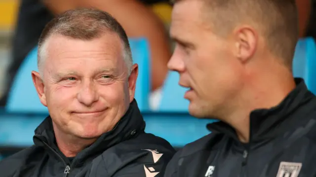 Stoke boss Mark Robins smiling in the dugout