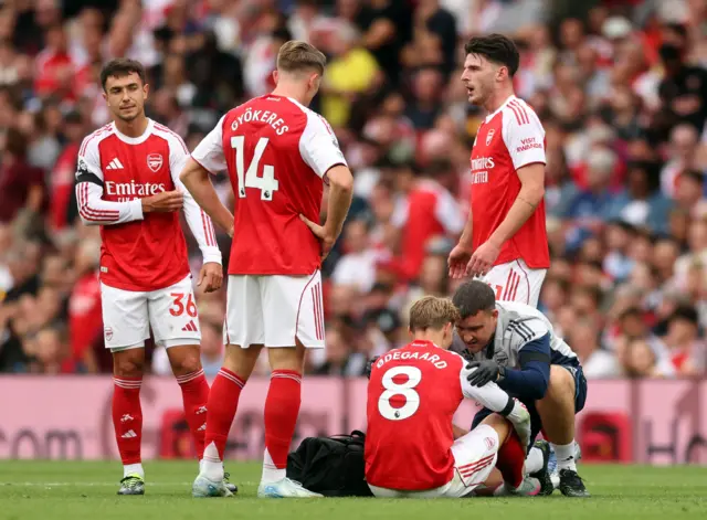 Odegaard sits on the floor being tended to by the physio as teammates watch on